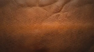Macro de la flor de un cuero de vaca curtido en marrón, con luz lateral cálida que marca el poro y las arrugas naturales