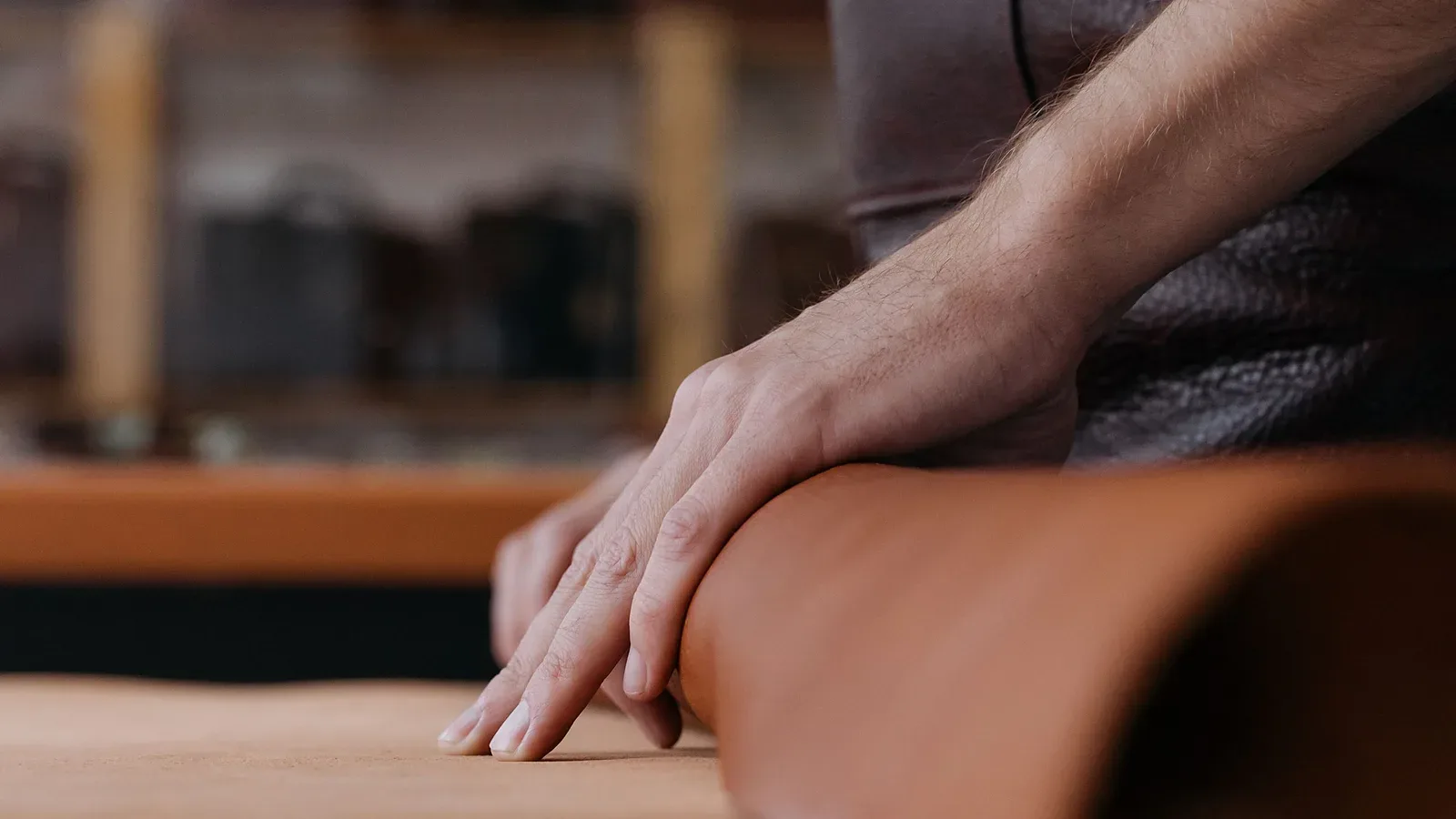 Mano apoyada sobre un rollo de cuero liso color suela en un banco de taller