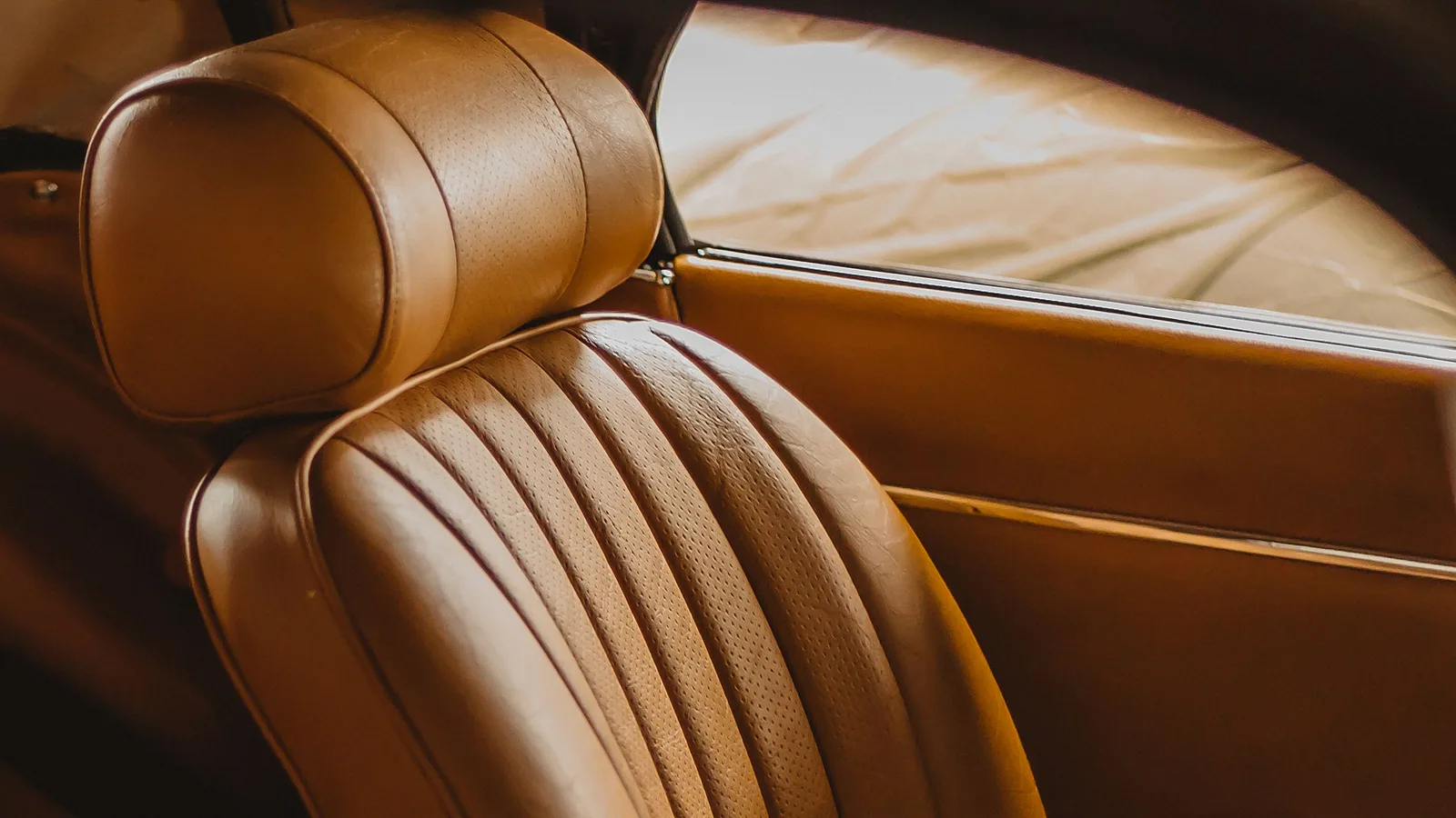 Cuero para tapizado de autos en un asiento clásico color miel: apoyacabeza, respaldo con pliegues cosidos y franjas perforadas, y la puerta forrada en el mismo cuero