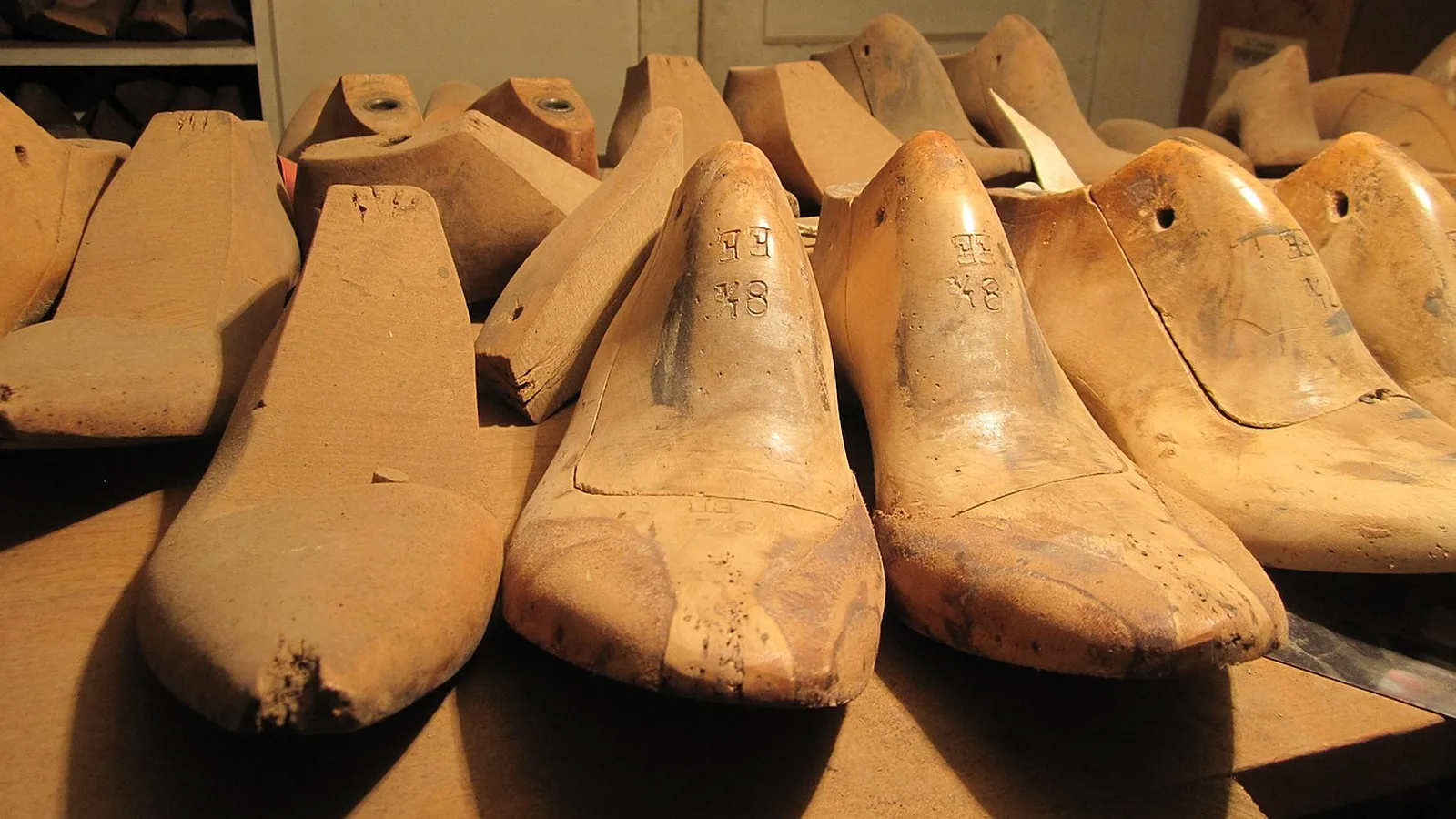 Hormas de madera usadas, con la talla grabada a mano, en fila sobre la mesa de un taller de zapatería